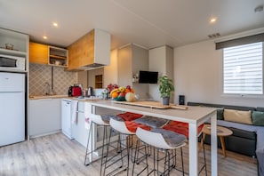 Una cocina moderna con una isla central, taburetes de bar, horno empotrado y televisor de pantalla plana.