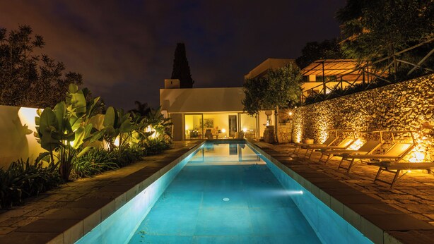 A nighttime swimming pool with lounge chairs and a building with a glass facade.