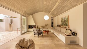 A modern interior with a curved ceiling, a round skylight, a seating area with a sofa and chairs, and a large painting on the wall.