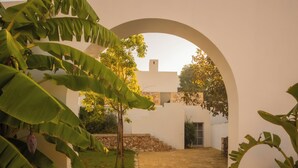 An arched pathway leading to a building with a stone wall and a small garden area.