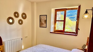 A bedroom with a bed, a radiator, a window with a view, and wall decorations.