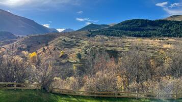 A mountainous landscape with a wooden fence, grassy areas, and trees.