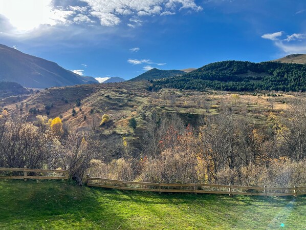 A mountainous landscape with a wooden fence, grassy areas, and trees.