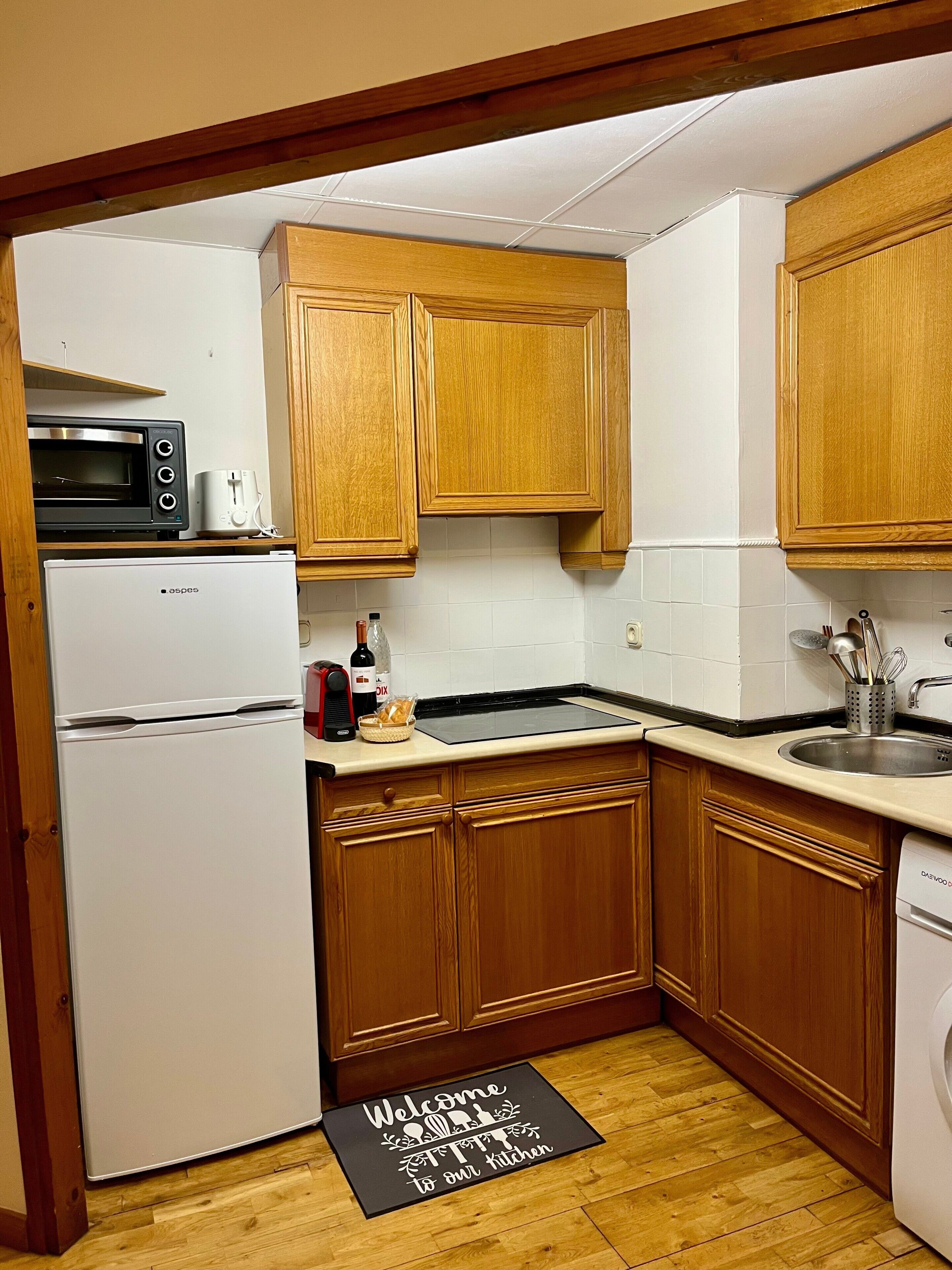 Una cocina con gabinetes de madera, un microondas, un tostador, un lavamanos y un refrigerador.