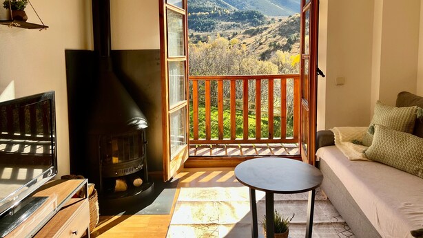 A cozy room with a fireplace, a sofa, a small table, and a balcony with a scenic view.
