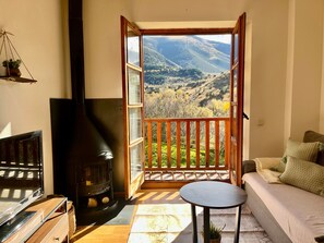 A cozy room with a fireplace, a sofa, a small table, and a balcony with a scenic view.