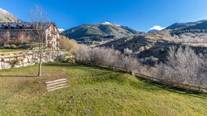 A mountain landscape with a stone building, a wooden fence, and a clear sky.