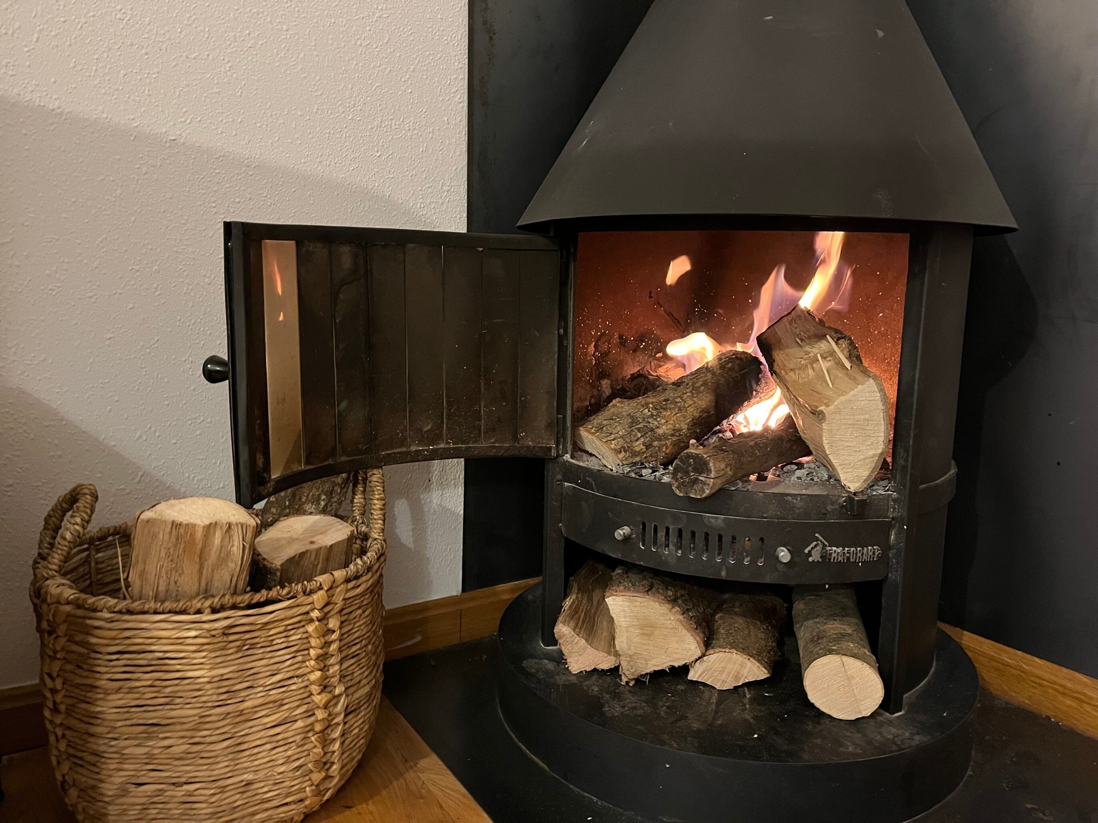 Un poêle à bois avec des bûches, un panier de bois de chauffage et une porte.