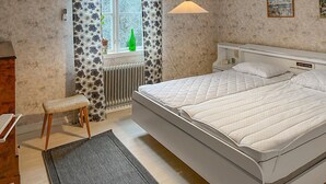 Ein Schlafzimmer mit einem großen Bett, einem Nachttisch, einem Heizkörper, einem Fenster mit Vorhängen und einer Pendelleuchte.