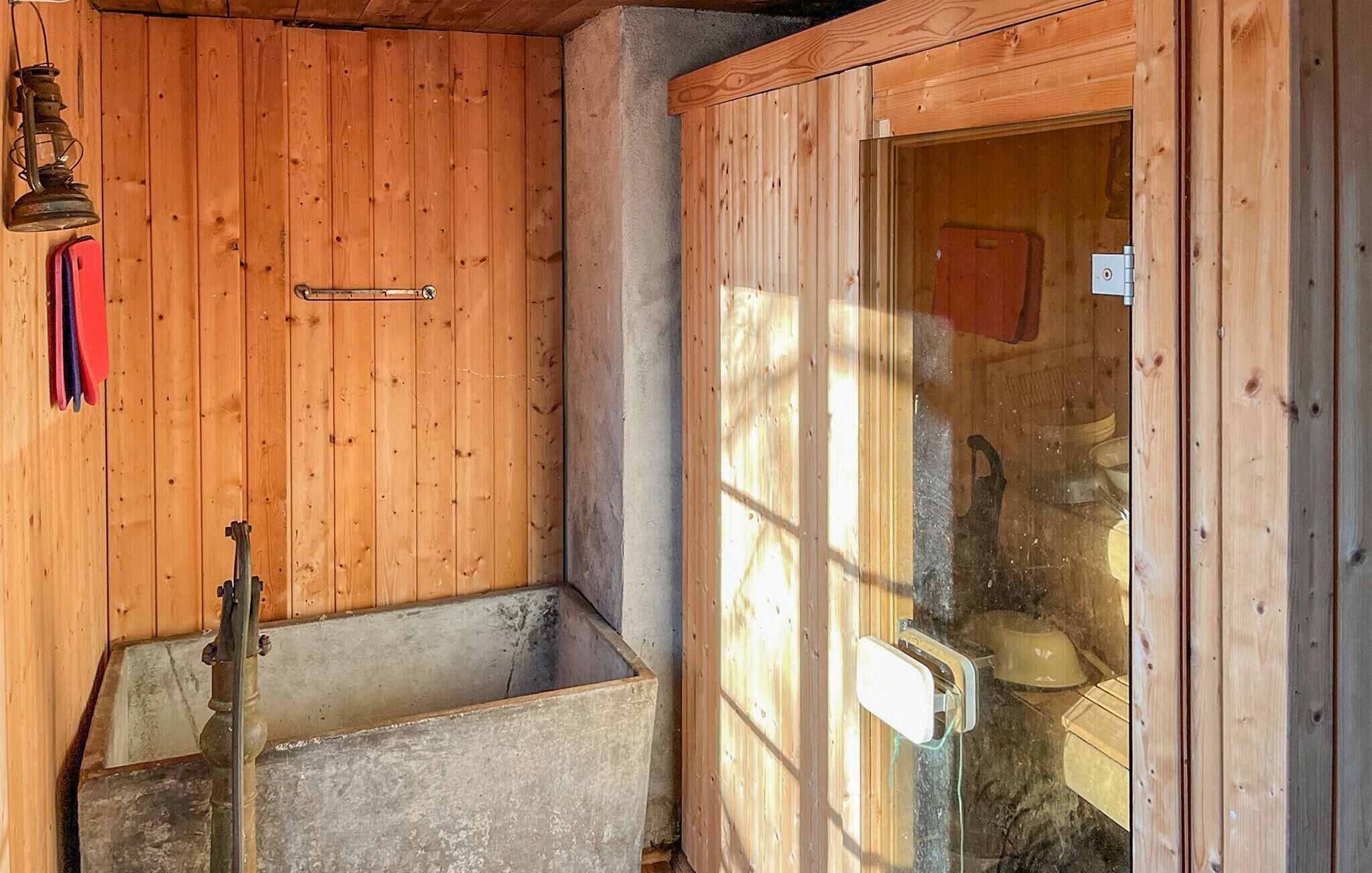 Interior de una cabaña de madera con una puerta de madera, un tirador de metal, un farol de metal y un objeto rojo colgando en la pared.