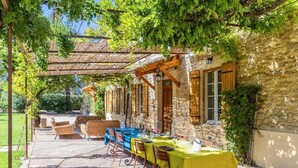 An outdoor patio with a table set for dining, covered by a pergola with vines, and stone walls. - Awesome home in Orsan (Orsan)