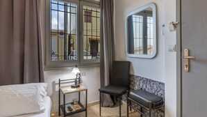Ein Hotelzimmer mit Bett, Schreibtisch mit Lampe, Stuhl, einem Fenster mit Vorhängen, einem Spiegel und einer Tür.