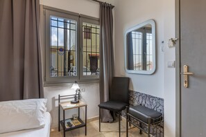 Une chambre d’hôtel avec un lit, un bureau avec une lampe, une chaise, une fenêtre avec des rideaux, un miroir et une porte.