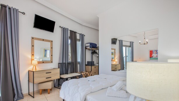 Une chambre d’hôtel comprenant un lit, un bureau avec une chaise, un téléviseur fixé au mur et un miroir.