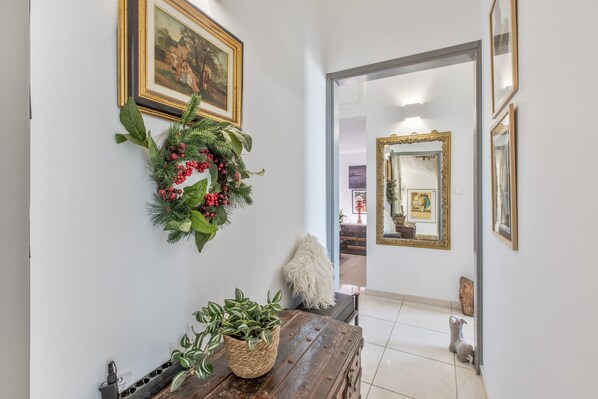 Un couloir avec un banc en bois, une plante en pot, une couronne et un miroir.
