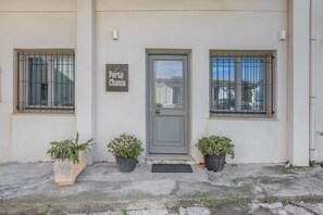Un bâtiment avec une porte grise, deux plantes en pot de chaque côté et une enseigne au-dessus de la porte.