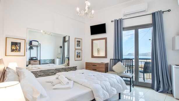 A hotel room with a bed, a chair, a TV, a mirror, and a balcony with curtains.