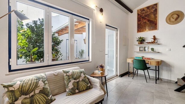 A room with a sofa, a desk, a chair, a window with plants, and a painting on the wall. - Tiny Home 'Casa Das Cantonas Valada' with Shared Pool, Wi-Fi and Air Conditioning (Valada)