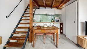 A kitchen with a wooden staircase, a dining table with chairs, and a television. - Tiny Home 'Casa Das Cantonas Valada' with Shared Pool, Wi-Fi and Air Conditioning (Valada)