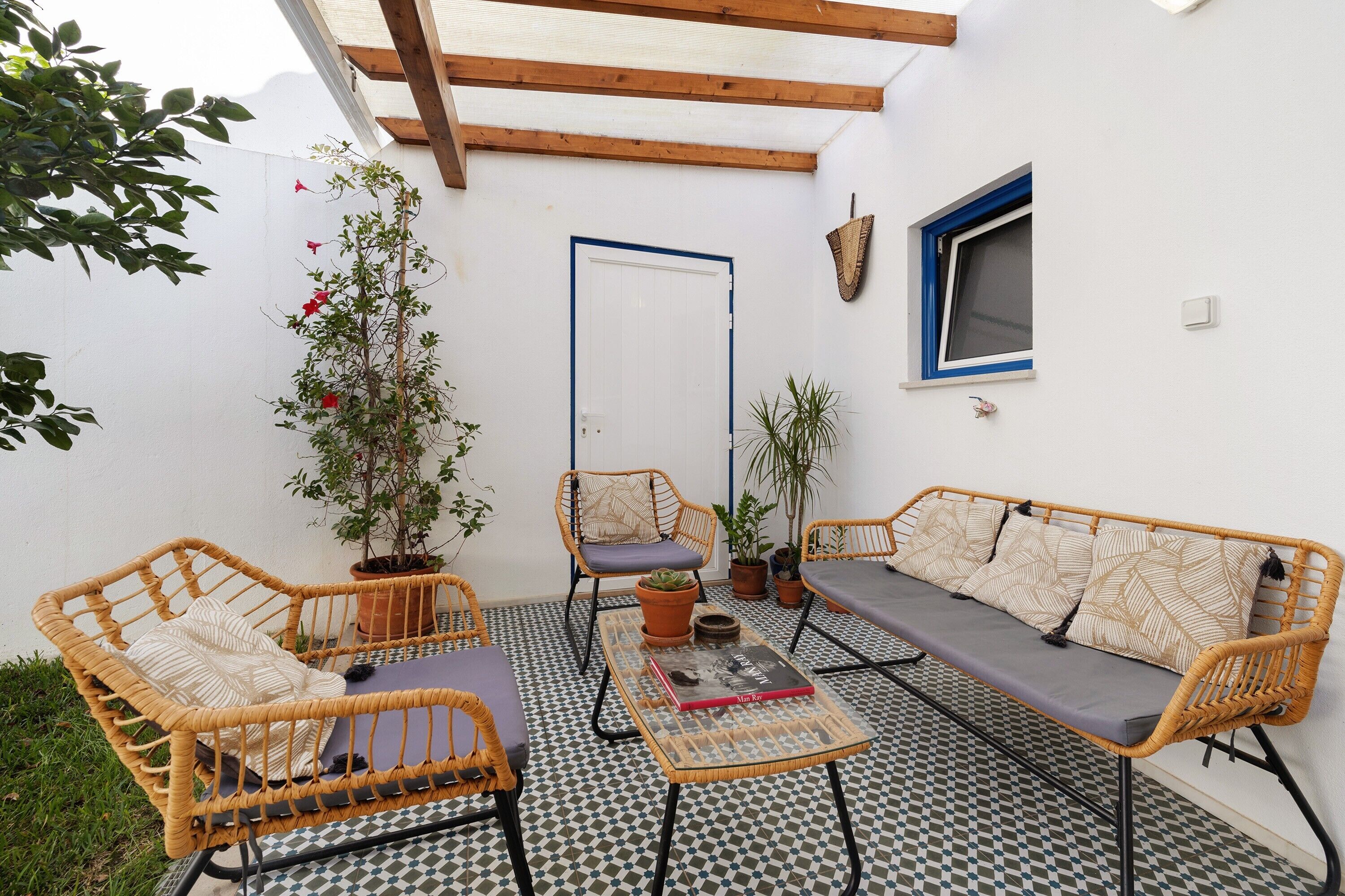 Une terrasse dotée de meubles en osier, d’un sol à carreaux et de plantes en pot.