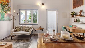 A modern living room with a sofa, a coffee table, a bookshelf, and a window with a view of greenery. - Tiny Home 'Casa Das Cantonas Valada' with Shared Pool, Wi-Fi and Air Conditioning (Valada)