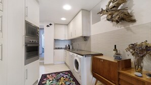 A modern kitchen with a built-in oven, washing machine, and a wooden countertop.