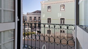 A balcony with a wrought iron railing, a view of a street with buildings, and a clear sky.