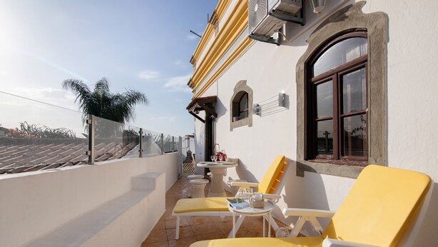 A balcony with yellow chairs and a table, a window with a red frame, and an air conditioning unit. - Holiday Home 'Solar Da Tirosa' with Private Pool, Private Terrace and Wi-Fi (Boliqueime)