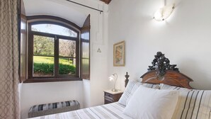 A bedroom with a bed, a bedside table with a lamp, a bench, a window with a view of greenery, and a wall-mounted light fixture. - Holiday Home 'Solar Da Rosa' with Private Pool, Private Terrace and Wi-Fi (Boliqueime)