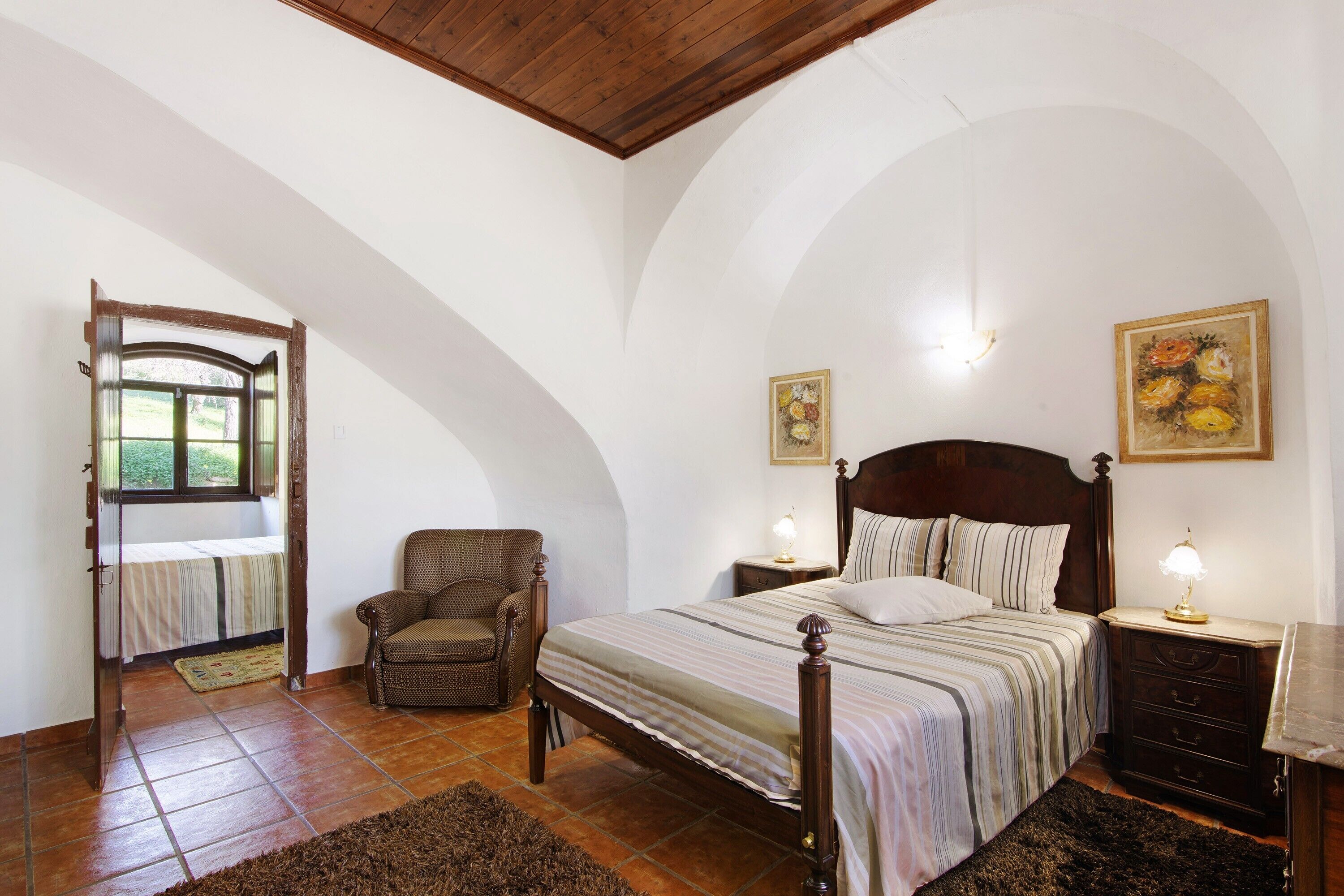 Une chambre à coucher comprenant un lit, une chaise, des tables de chevet et des œuvres d’art murales.