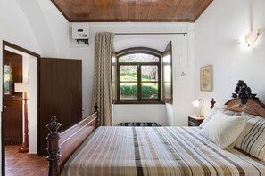 Une chambre à coucher avec un lit, une fenêtre avec des rideaux, une table de chevet avec une lampe et un plafond en bois.