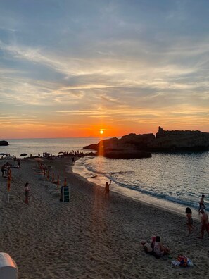 Una playa con gente, sombrillas y un atardecer.
