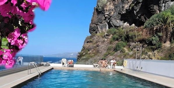 Ein Poolbereich mit Liegestühlen und Blick aufs Meer.