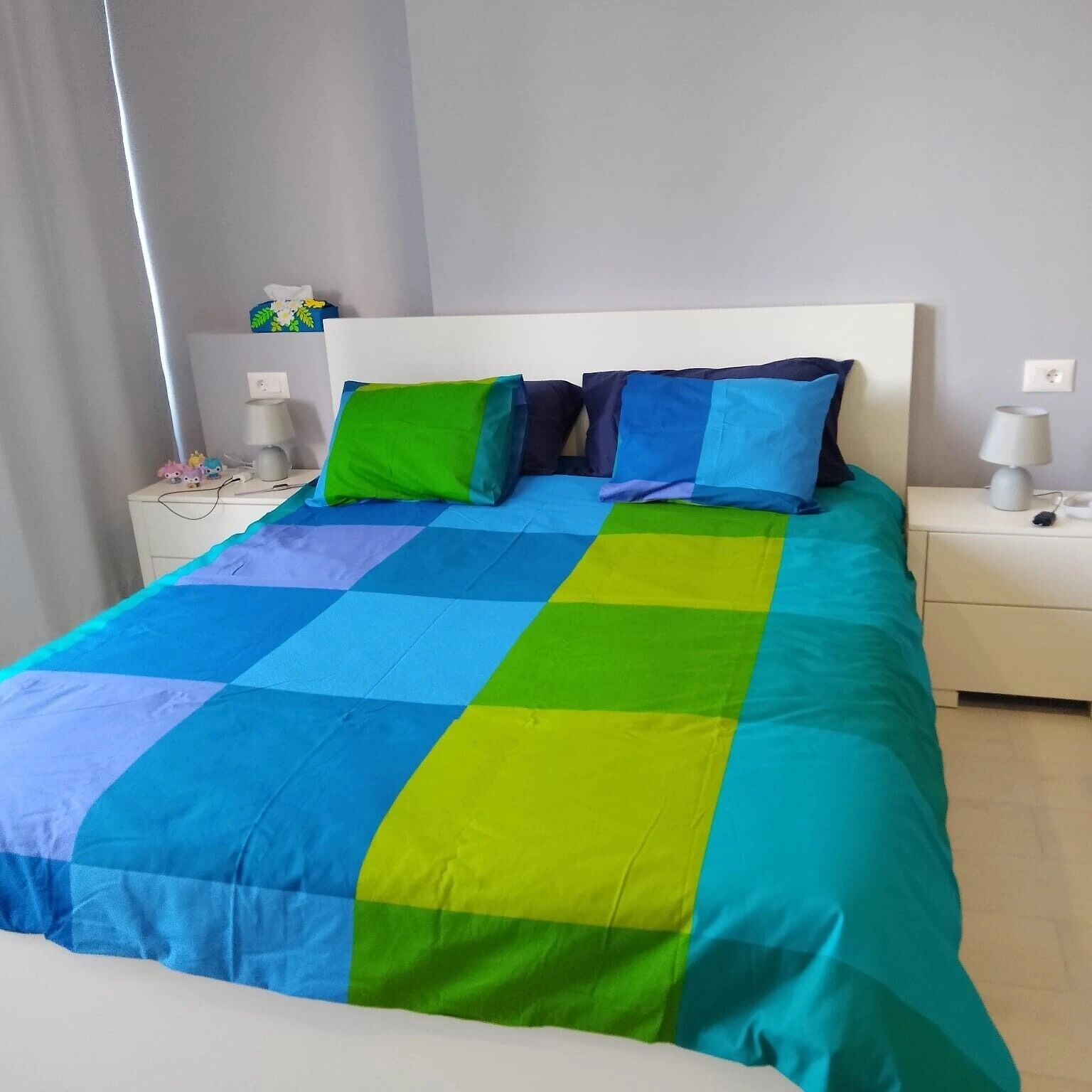 Una cama con un colcha multicolora, un cabecero blanco y dos mesitas de noche con lámparas.