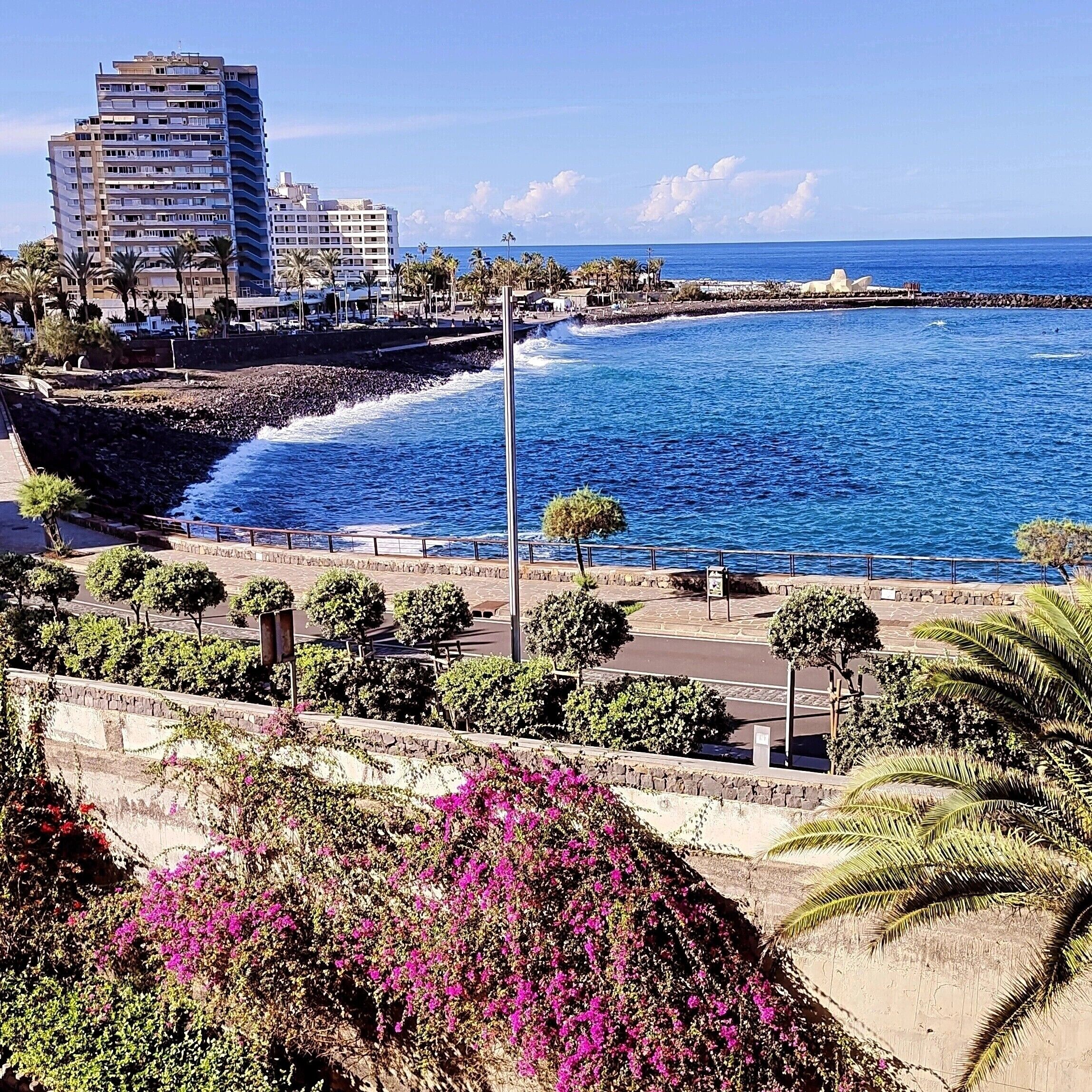 Un paisaje urbano costero con un edificio destacado, un paseo marítimo y una vista despejada del mar.