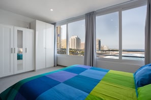 Ein Schlafzimmer mit einem großen Bett, einem weißen Kleiderschrank und Blick auf Stadt und Meer.