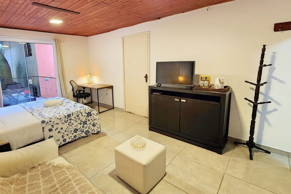 Una camera d'albergo con un letto, una poltrona, una TV, una scrivania e un balcone con vista.