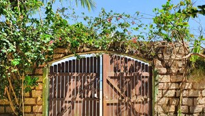 A wooden gate with a metal lock, set against a stone wall with climbing plants. - Villa Daniella - Beach Homes (Florianópolis)