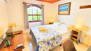 A bedroom with a bed, a desk with a laptop, a chair, a window with curtains, a bedside lamp, and a wall-mounted shelf. - Villa Daniella - Beach Homes (Florianópolis)