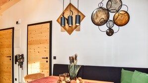 Een kamer met een houten deur, een wandlamp, een decoratief object aan de muur, een tafel met een rode tafelkleed en een groene kussen op een zwarte bank.