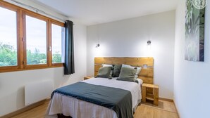 Une chambre à coucher avec une tête de lit en bois, un grand lit recouvert d’une couvre-lit aux couleurs sombres et claires, deux tables de chevet et une fenêtre avec des rideaux.