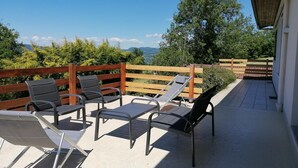 Une terrasse avec des sièges extérieurs, une clôture en bois et une vue sur la verdure et les montagnes.