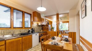 Une cuisine avec des meubles en bois, un pare-feu en carreaux, une table à manger avec des chaises et une vue sur l’extérieur.