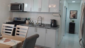 Una cocina compacta con armarios blancos, microondas, cafetera y comedor con mesa y sillas.