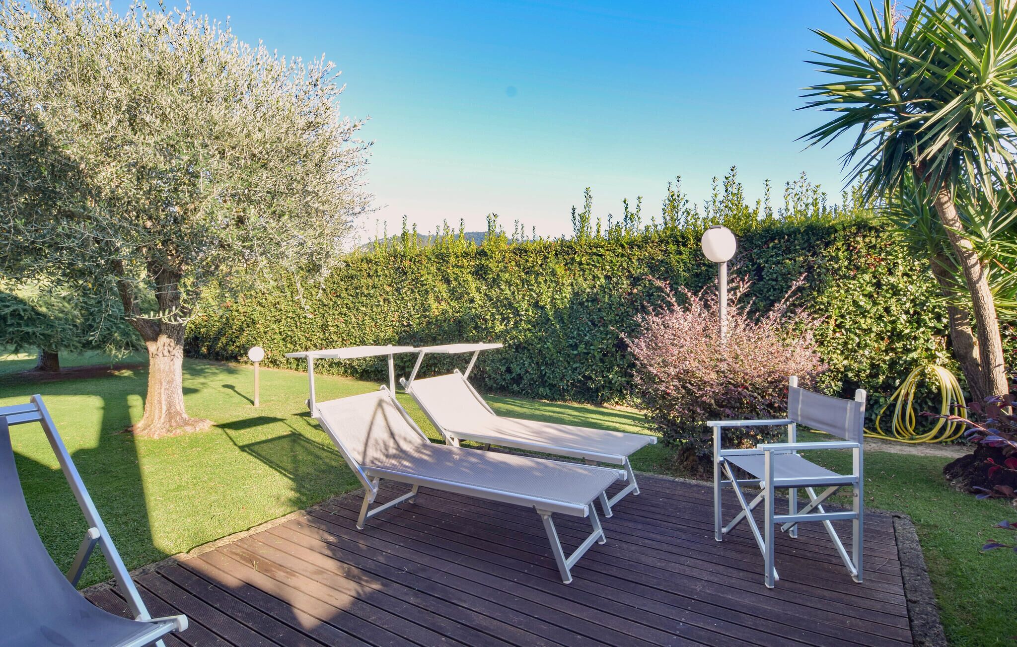 A deck with two lounge chairs and a table, surrounded by a well-maintained garden with various plants and a hedge.