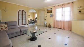 Una sala de estar con un sofá, una mesa de centro de vidrio y una zona de comedor al fondo.