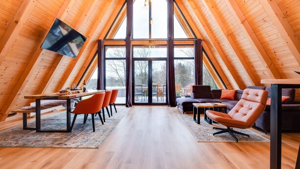 Un intérieur chaleureux en bois, doté de hauts plafonds, d’un espace repas, de sièges et d’une grande fenêtre.
