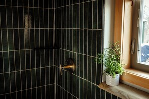 Een hoek van een kamer met donkere betegelde muren, een deur met een messing knop en een potplant op een vensterbank.