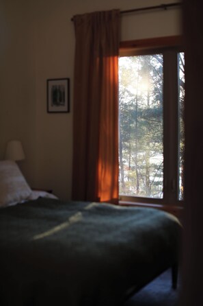 Een kamer met een bed, een raam met gordijnen en een lijst met een afbeelding aan de muur.