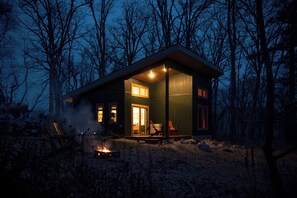 Een chalet met een vuurkuil, een houten terras en een overdekte veranda met stoelen.